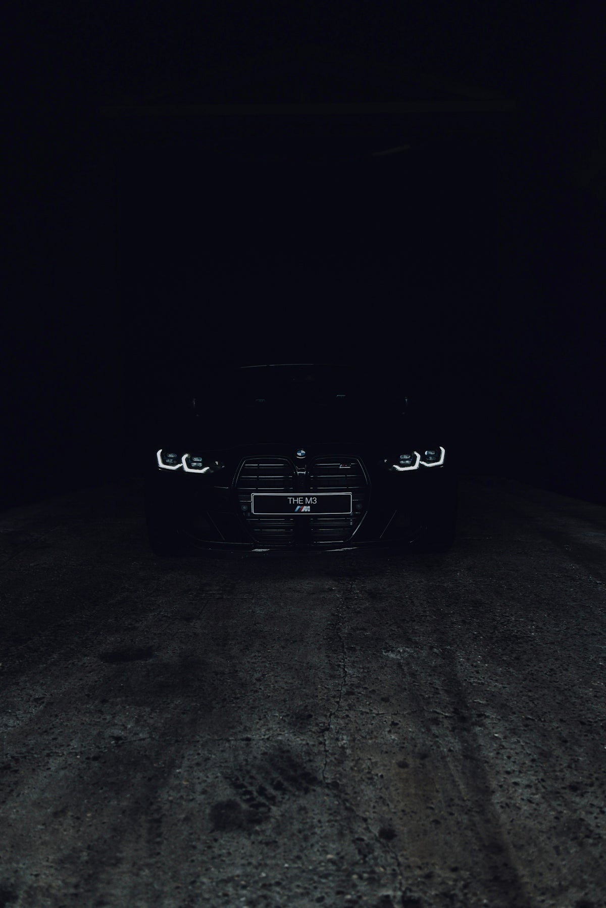 A black car with illuminated headlights on a dark concrete surface