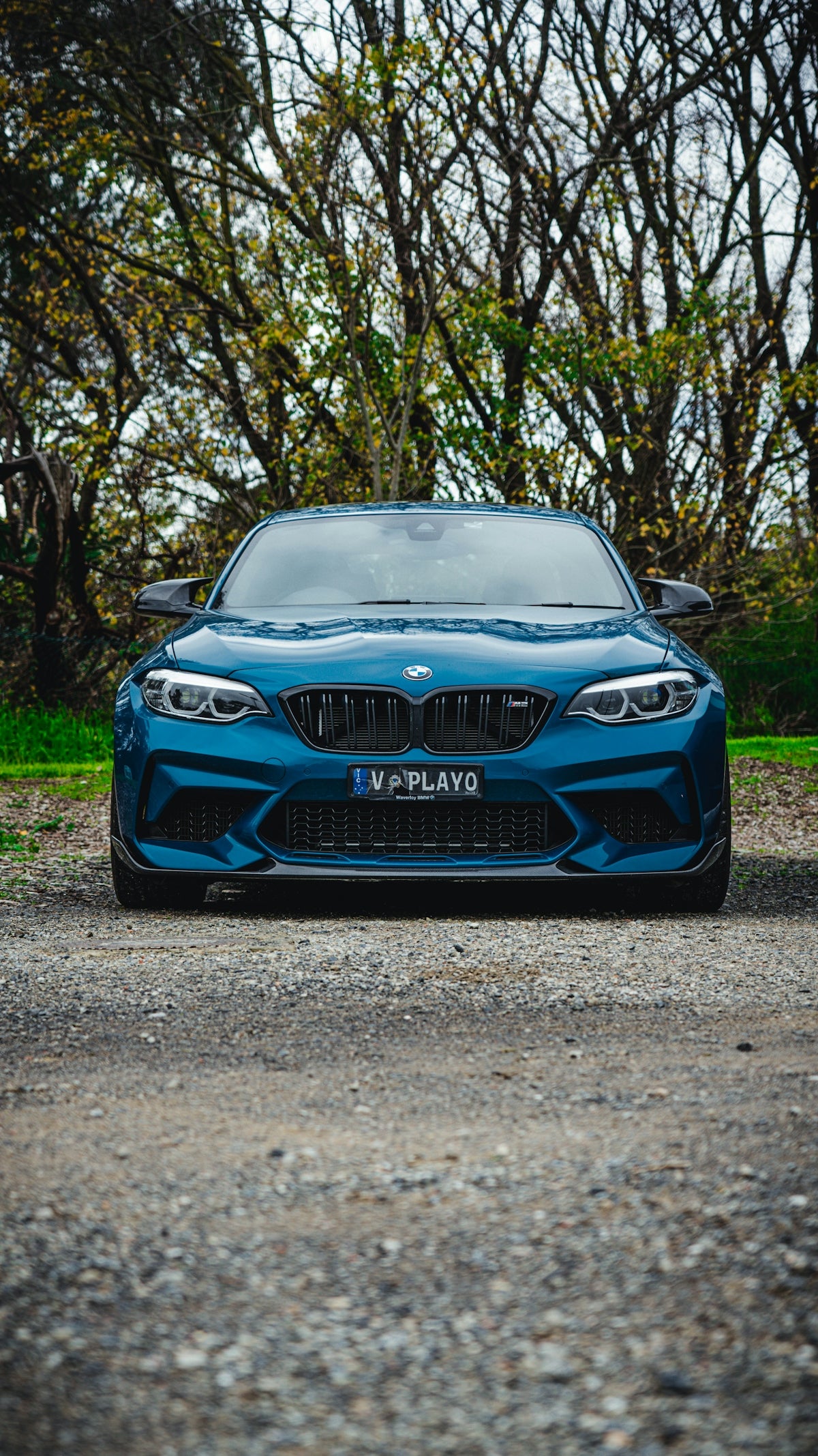 a blue car parked on a gravel road with trees in the background