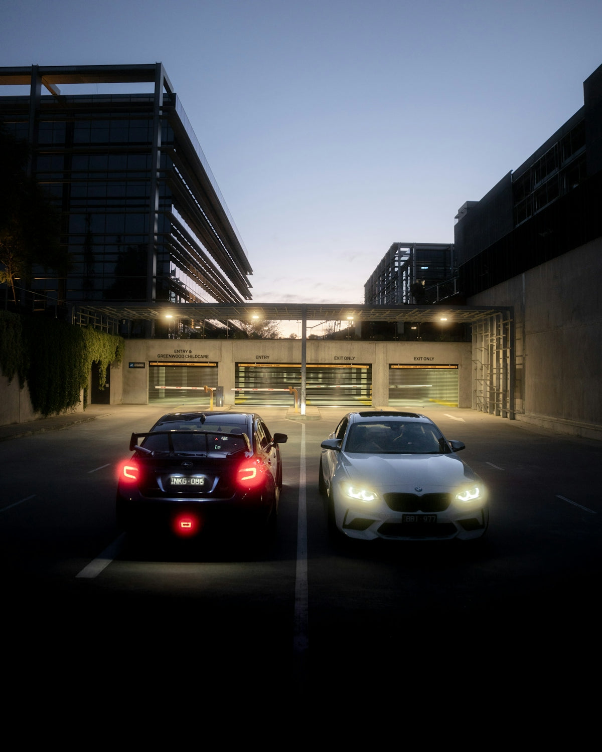Two cars parked in front of modern buildings at dusk