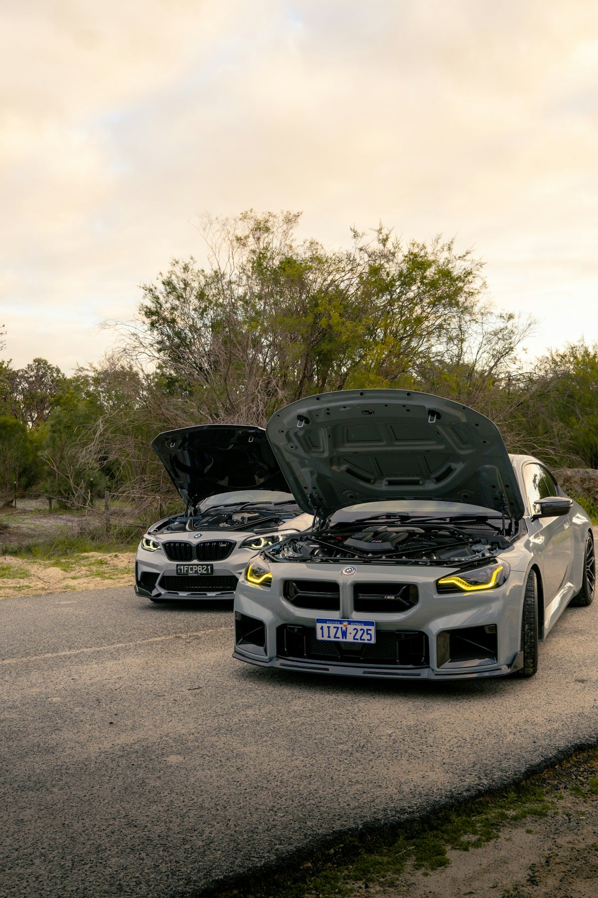 Two sleek cars with open hoods parked outdoors.