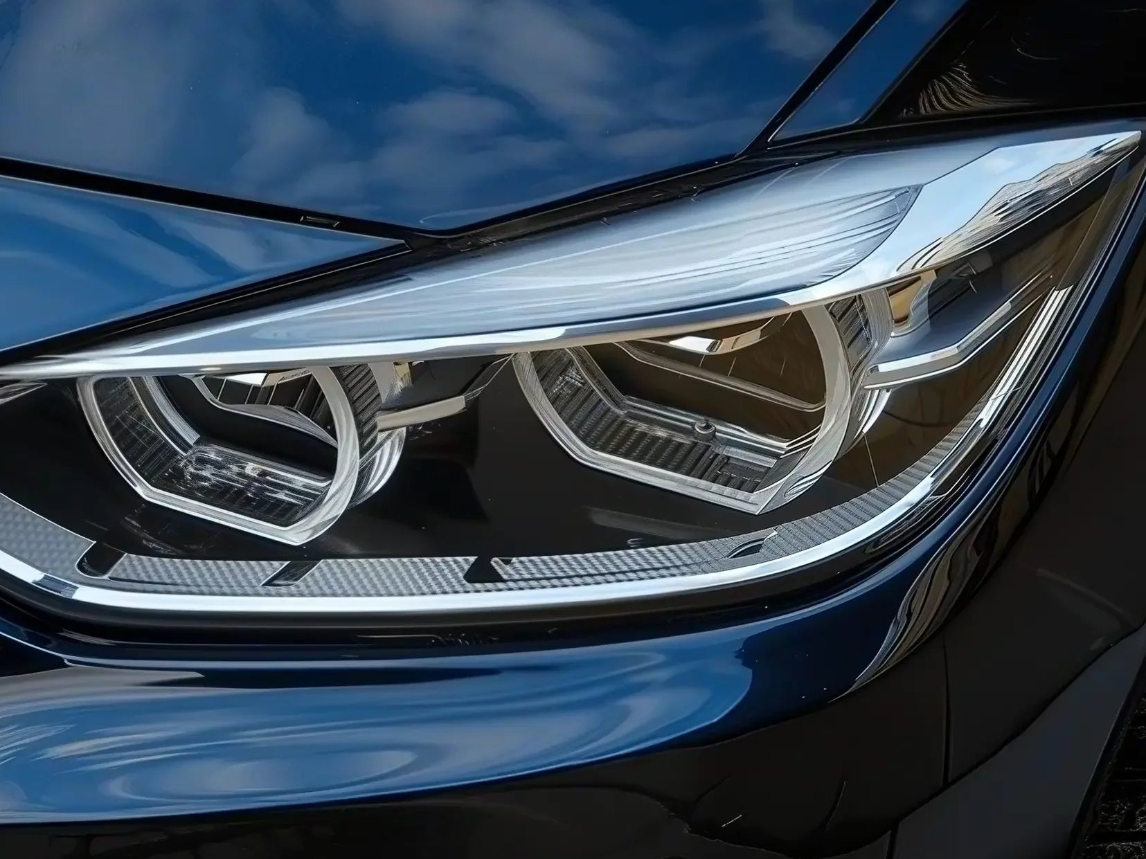 Close-up of modern BMW headlight with clear lens and blue car hood reflections