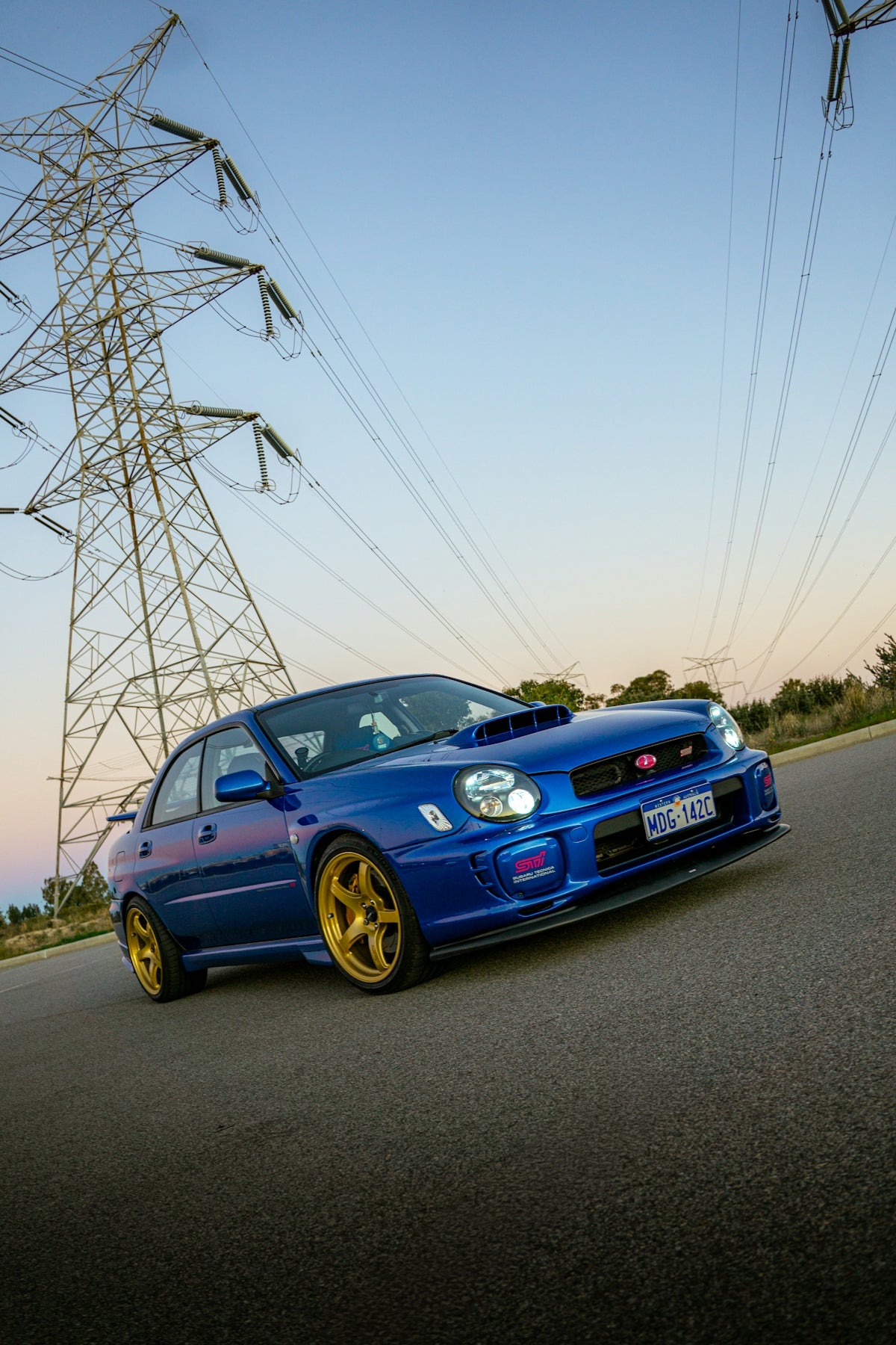 Blue sports car with gold wheels near power lines.